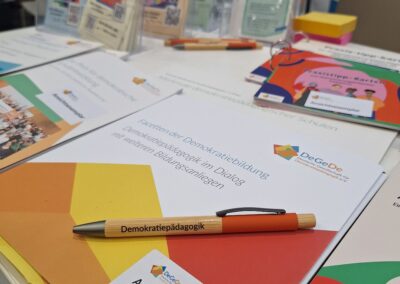 Kugelschreiber mit der Aufschrift "Demokratiepädagogik" auf einem Tisch mit Infomaterial