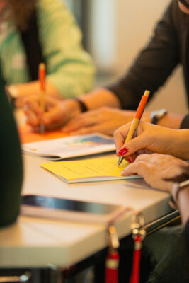 Man sieht Hände, die Stifte halten und auf bunte Zettel schreiben