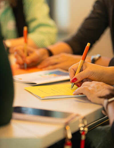 Man sieht Hände, die Stifte halten und auf bunte Zettel schreiben