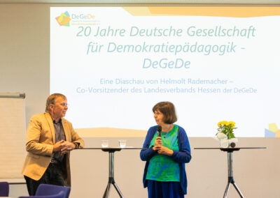 Zwei Personen stehen vor einer Wand mit angestahlter Power Poit Presentation