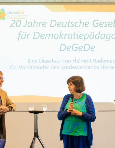 Zwei Personen stehen vor einer Wand mit angestahlter Power Poit Presentation